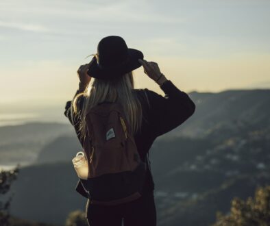 woman in gray hoodie and black pants wearing black hat standing on top of mountain during